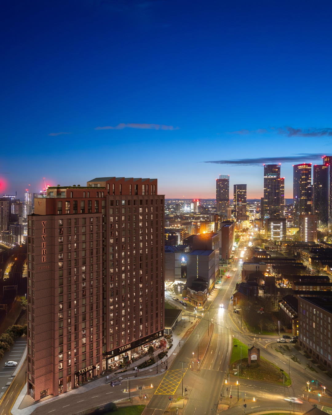 Architectural CGI of VIVERE Residences at Manchester Waters, showing the illuminated red-brick residential tower against the Manchester skyline at dusk, with city lights and surrounding high-rise buildings.